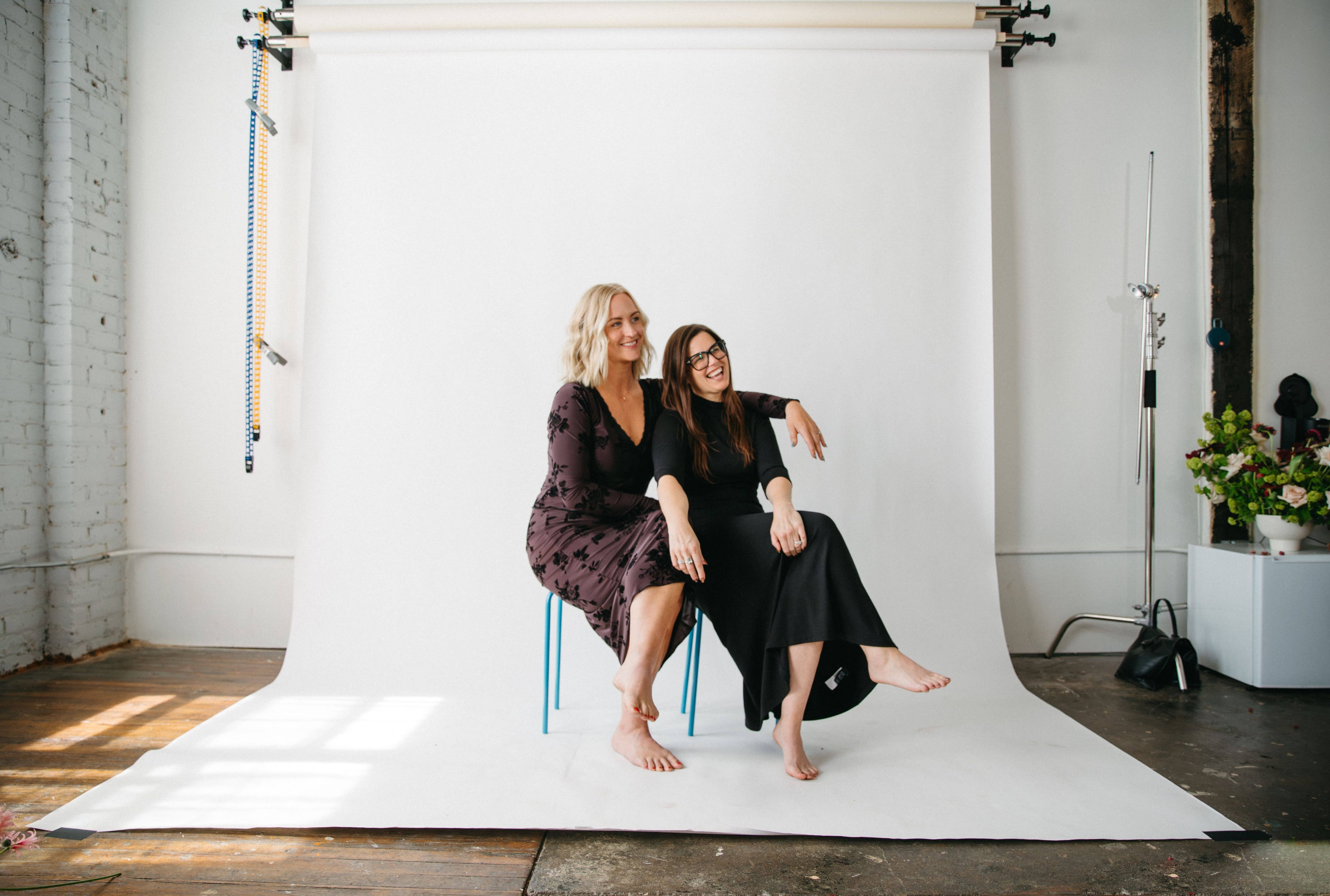 Marantz Collective owners Susan and Samantha laughing, sitting on stools in a photo studio with a white backdrop.