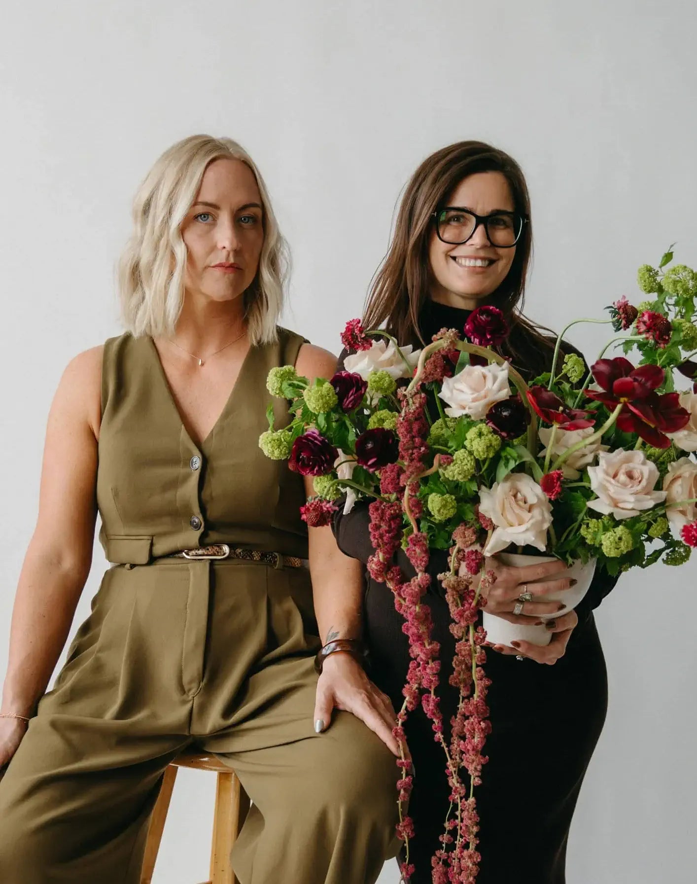 Marantz Collective founders Samantha, who is holding a floral arrangement, and Susan posing against a plain background.